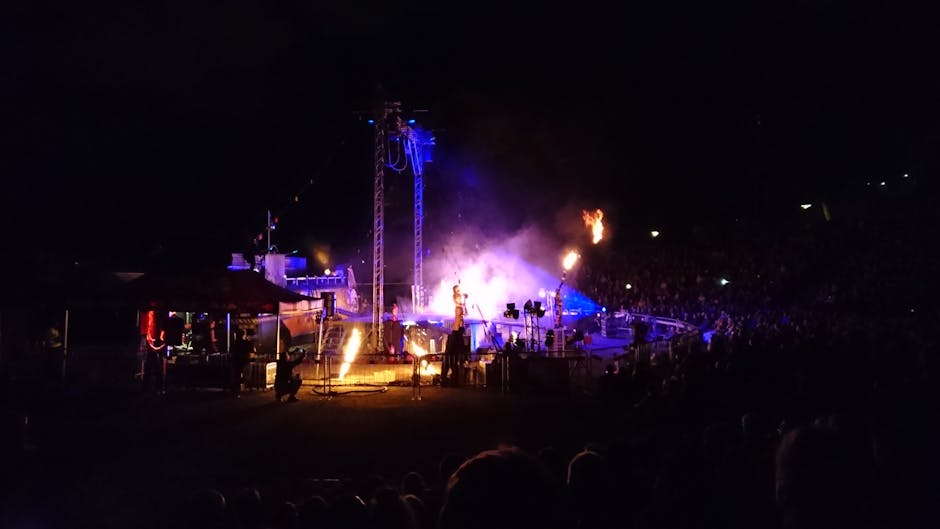 A vibrant live performance showcasing pyrotechnics, lights, and a large crowd at night.