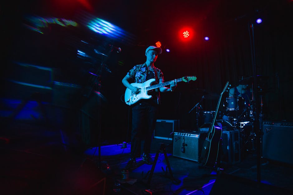 Musician playing electric guitar on stage with vibrant lighting during a live performance.
